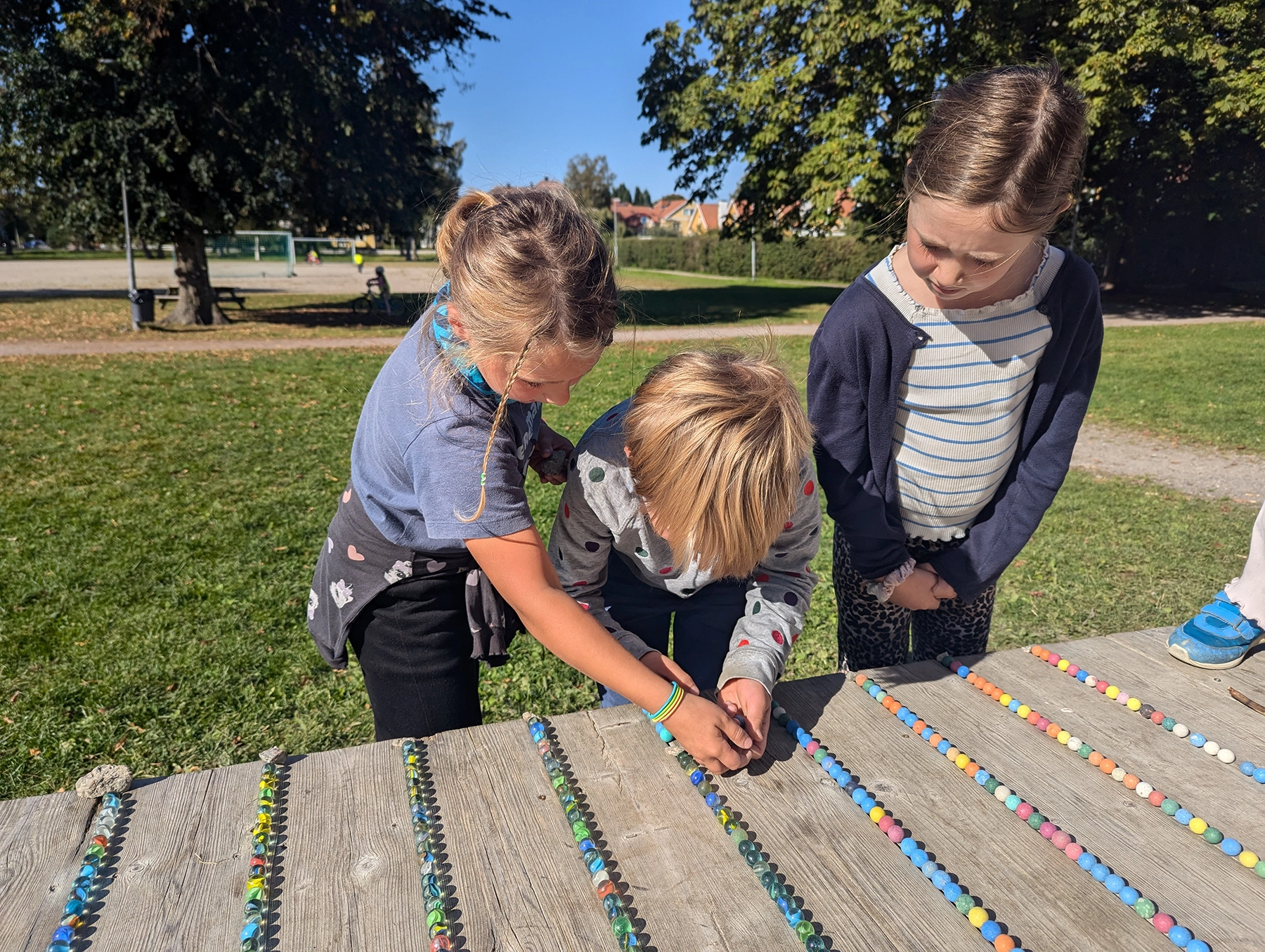 PXL_20240919_095312183 Tre skolelever leker med kulor på skolgården