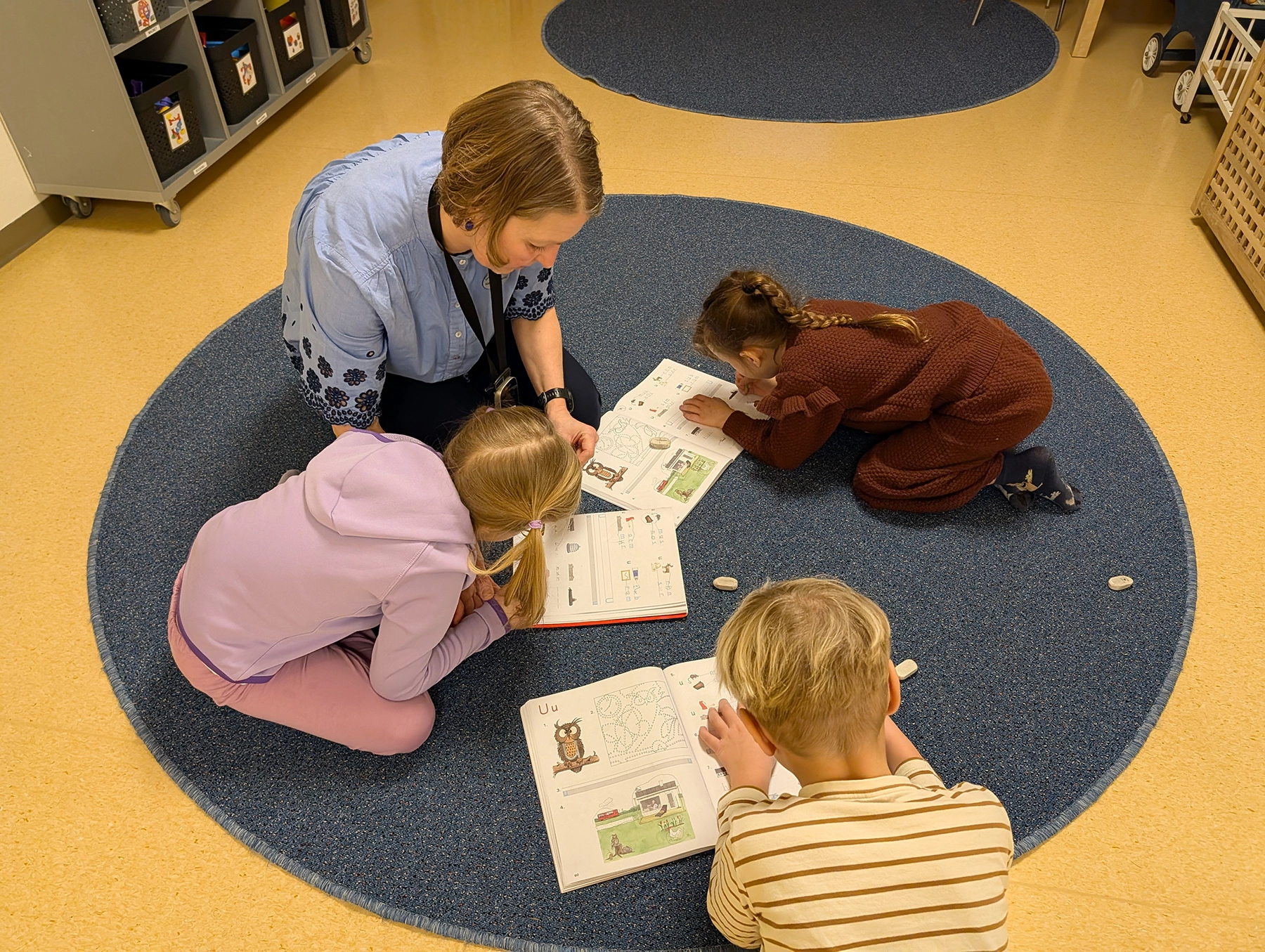 Skolelever och deras lärare sitter på golvet och läser i sina skolböcker